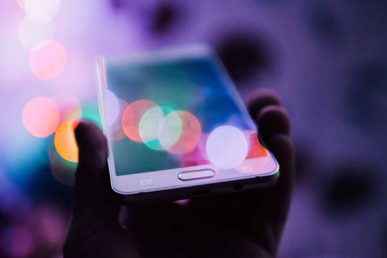 A hand holds a smartphone against blurred colored lights.