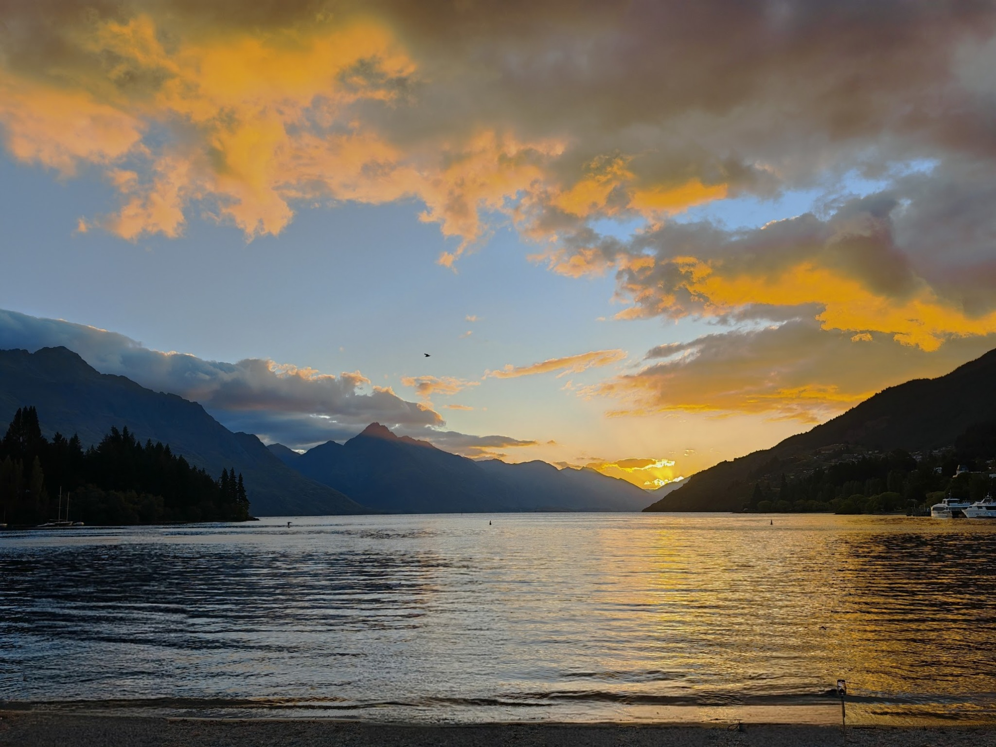 Golden sunset reflecting on Lake Wakatipu with mountains in the distance.