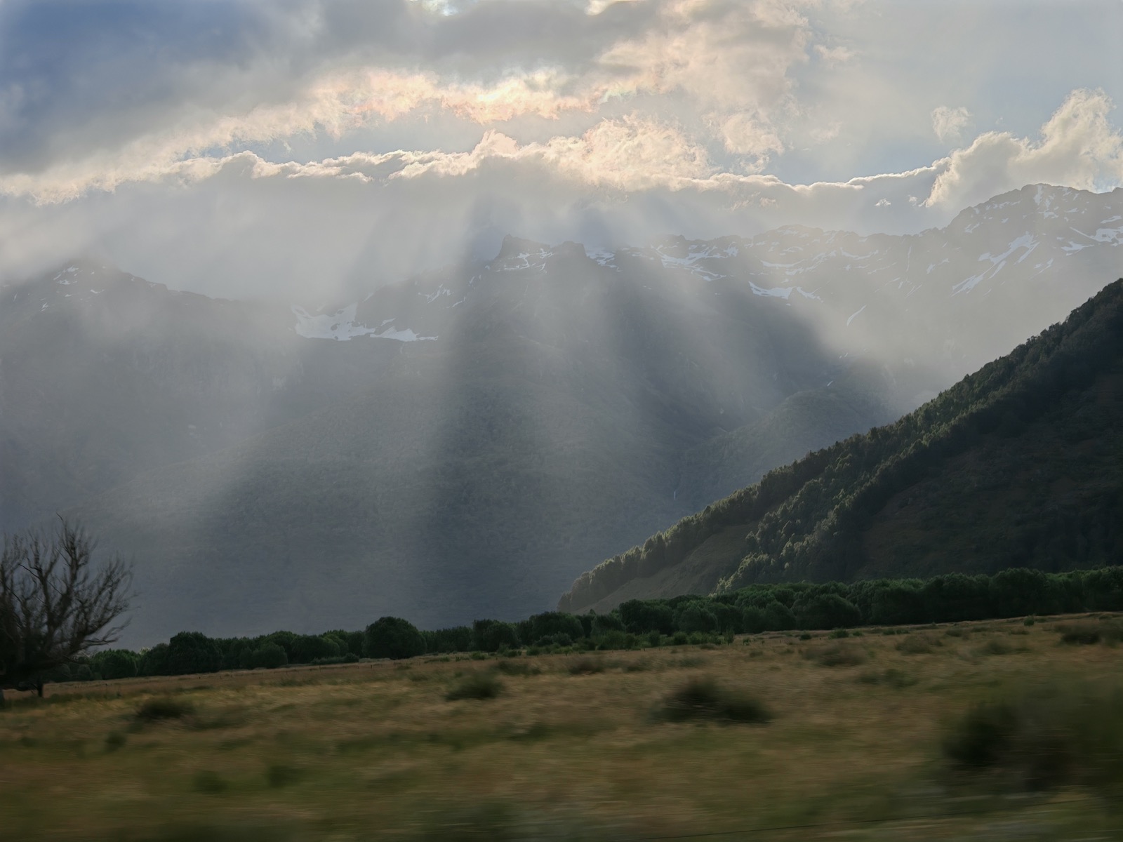 Misty ridge and sun rays over Glenorchy valley, captured from a moving vehicle.
