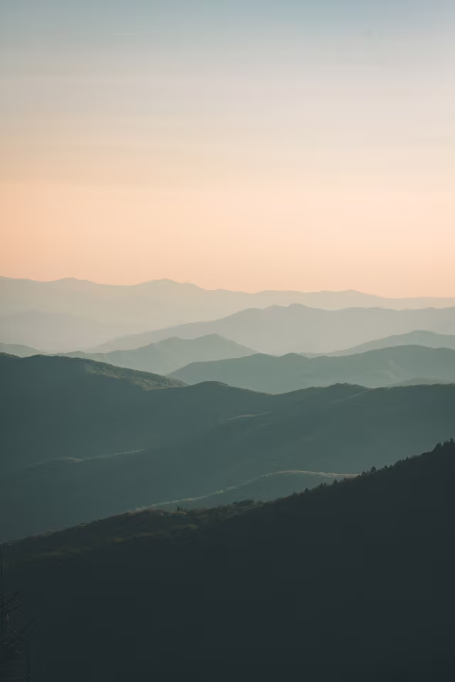Layered mountain ridges fading into a pale sunrise sky.